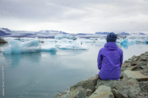 A young woman admires the blue ice in the ice lagoon of Iceland. Tourist with a red backpack