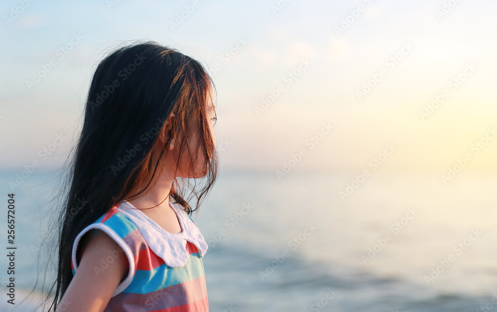 Portrait side view little Asian girl standing on beach at sunset light with looking out.