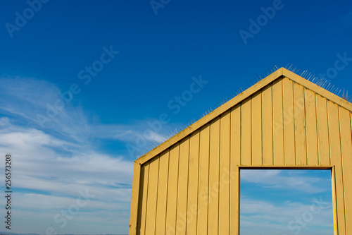 Yellow wooden gate with open door leading to beautiful sky 