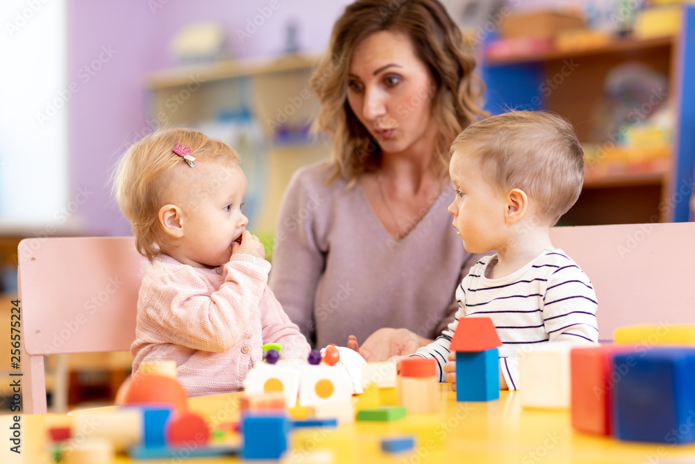 Fototapeta premium Children in kindergarten. Kids in nursery school. Little girl and boy preschoolers playing at table with teacher