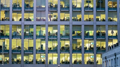 The exterior of an office block at night revealing the daily activity of office workers night themes of routines working late deadlines
