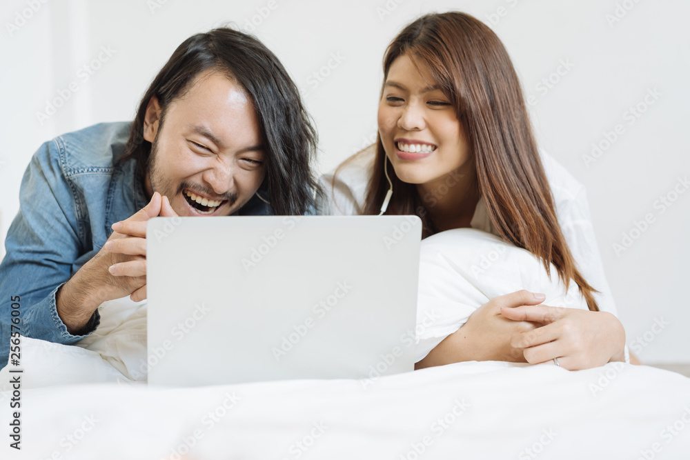 Young Asian couple watching movie with laptop in the bed Young Asian couple watching movie with laptop in the bed