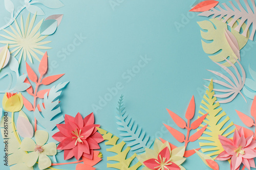 Colourful handmade tropical paper flowers and leaves on blue pastel background with copyspace in the middle, summer spring flower concept, papercraft origami idea © misskaterina