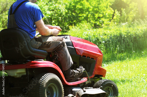 Fotografie Gardener driving a riding lawn mower in a garden