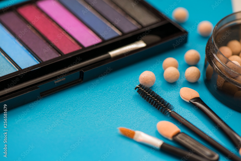 Top, up view of professional cosmetics, makeup background. Brushes, eye shadows, eyebrow pencils, powder, bronzing balls, mascara, red lipstick. Tools isolated on blue. Concept of get ready for party Top, up view of professional cosmetics, makeup background. Brushes, eye shadows, eyebrow pencils, powder, bronzing balls, mascara, red lipstick. Tools isolated on blue. Concept of get ready for party