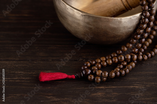 Tibetan singing bowl with mala beads on dark wooden background with copy space. Essential accessory for mindfulness or meditation.