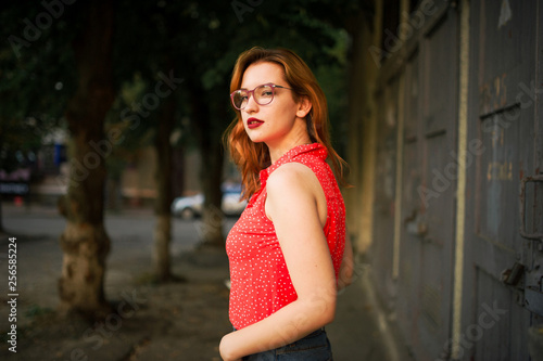 Attractive redhaired woman in eyeglasses, wear on red blouse and jeans skirt posing.