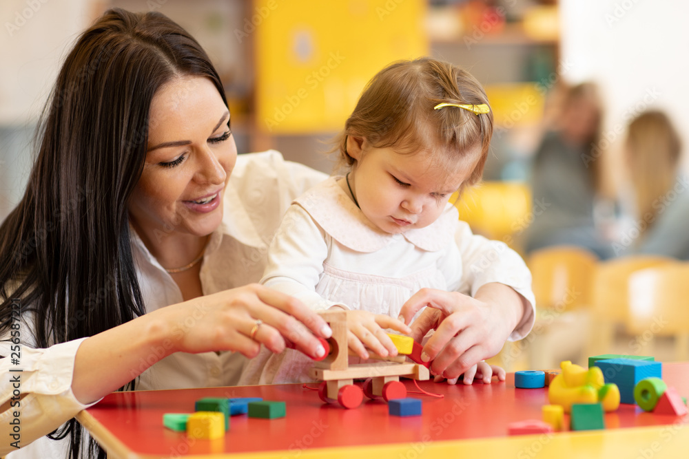 Kid with mother play with colorful wooden block toys on table in nursery Kid with mother play with colorful wooden block toys on table in nursery