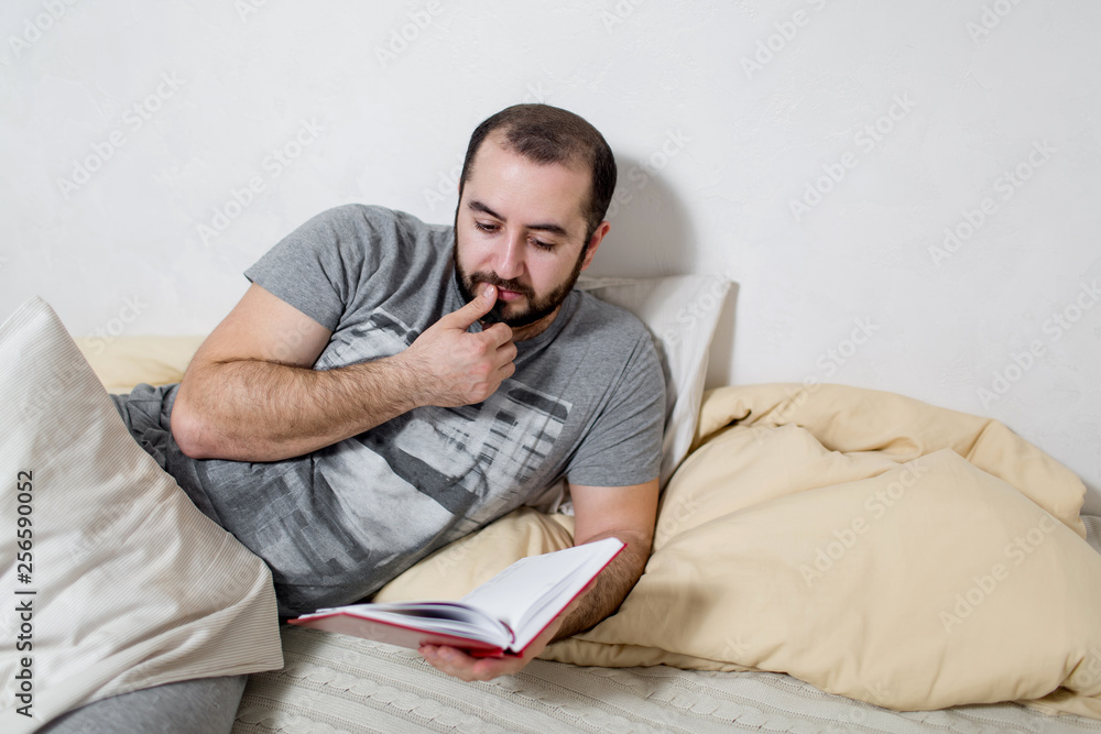 Young man pensive reads a book in the bedroom. White background. Young man pensive reads a book in the bedroom. White background.