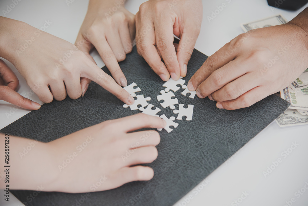 Close up Hands of business people holding jigsaw puzzle on a black file and some money in background, help support in teamwork concept. Close up Hands of business people holding jigsaw puzzle on a black file and some money in background, help support in teamwork concept.