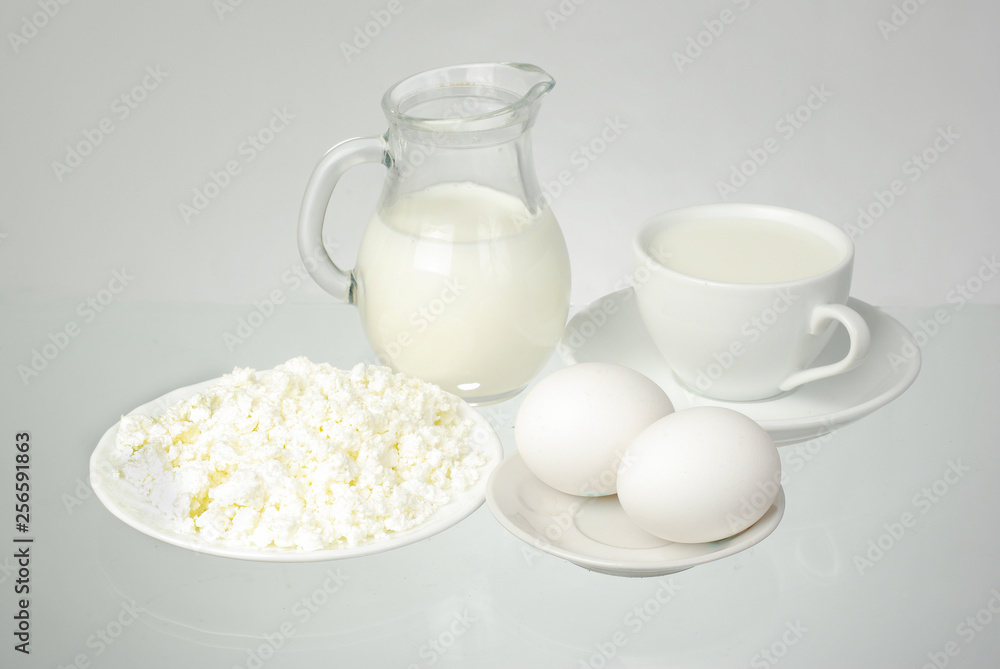 Milk in a white cup and jug, creative and eggs on a white background Milk in a white cup and jug, creative and eggs on a white background