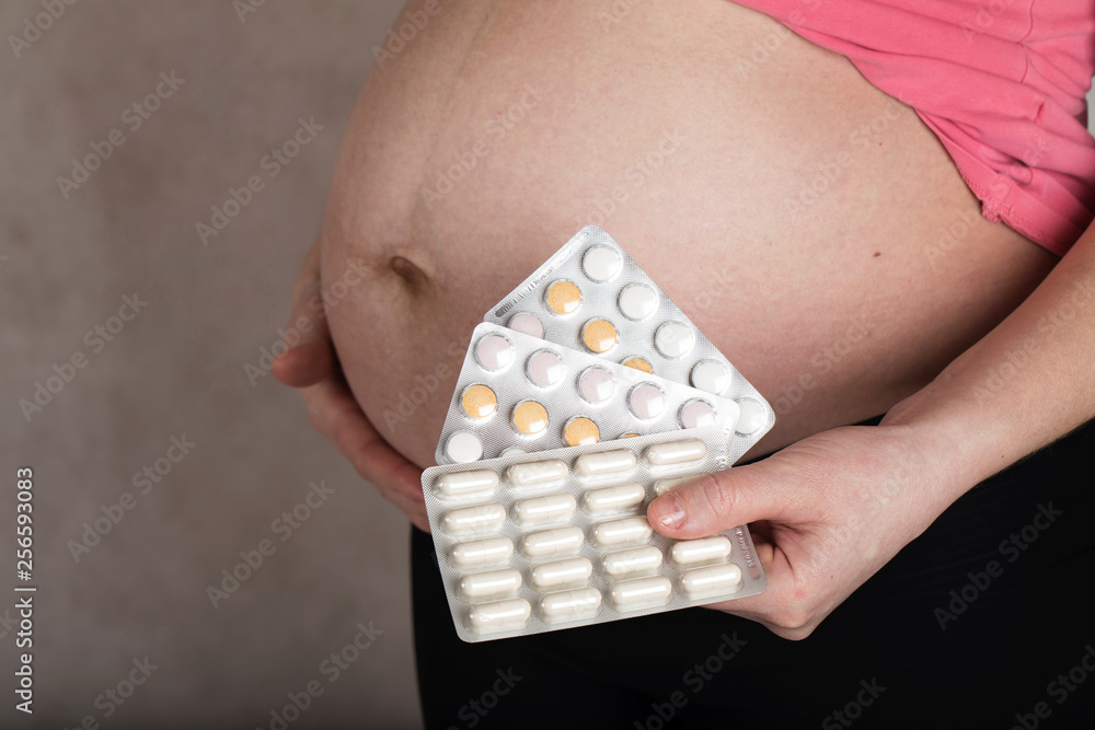 Obraz premium Young pregnant woman keeps films of pills close to her belly.