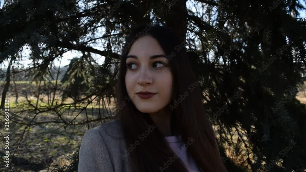 Portrait of a cute brunette girl in a coat under a pine tree in the dark.