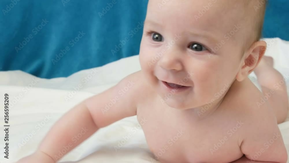 A two month old happy newborn baby lying on his stomach on the bed and experiences emotions to his mother. A baby laughs, talks, waves his arms. The child face close up view A two month old happy newborn baby lying on his stomach on the bed and experiences emotions to his mother. A baby laughs, talks, waves his arms. The child face close up view