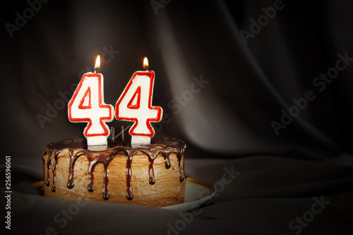 Forty four years anniversary. Birthday chocolate cake with white burning candles in the form of number Forty four. Dark background with black cloth photo