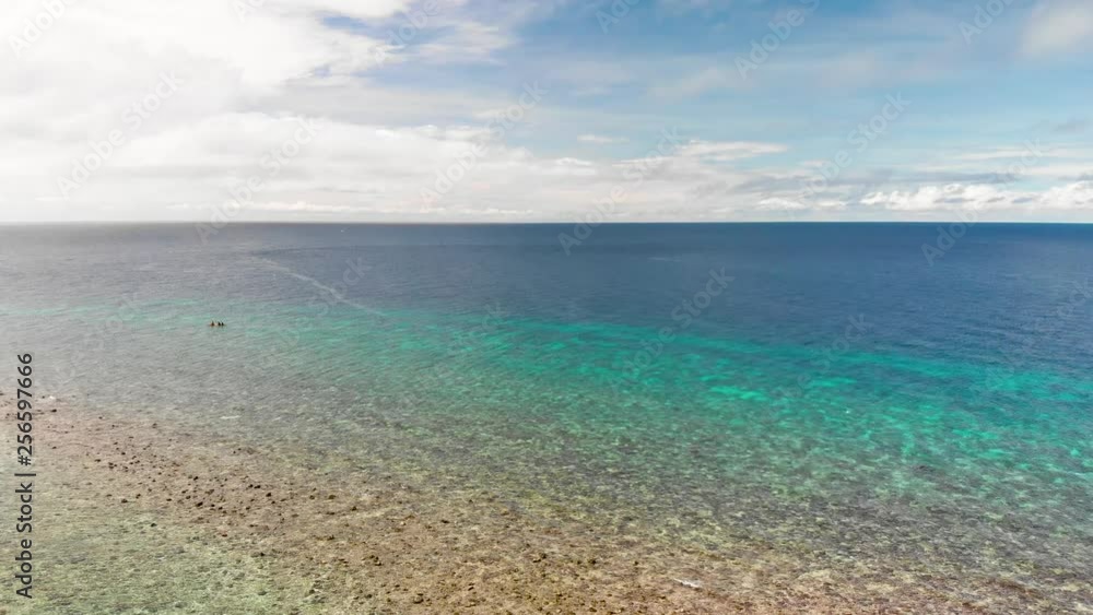 drone horizon shot of shallow blue tropical ocean under blue sky and white clouds as Philippine pump boat floats near the coral in the Pacific drone horizon shot of shallow blue tropical ocean under blue sky and white clouds as Philippine pump boat floats near the coral in the Pacific