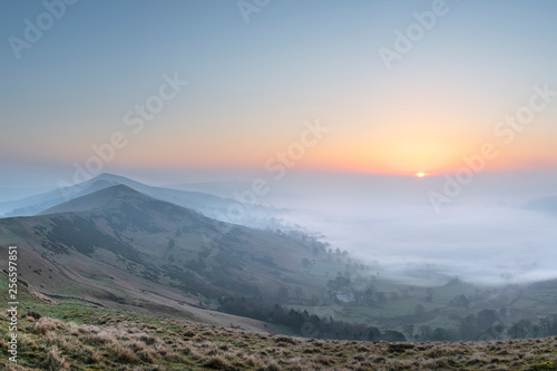 Stunning Winter sunrise landscape image of The Great Ridge in the Peak Distrit in England with a cloud inversion and mist in the Hope Valley with a lovely orange glow