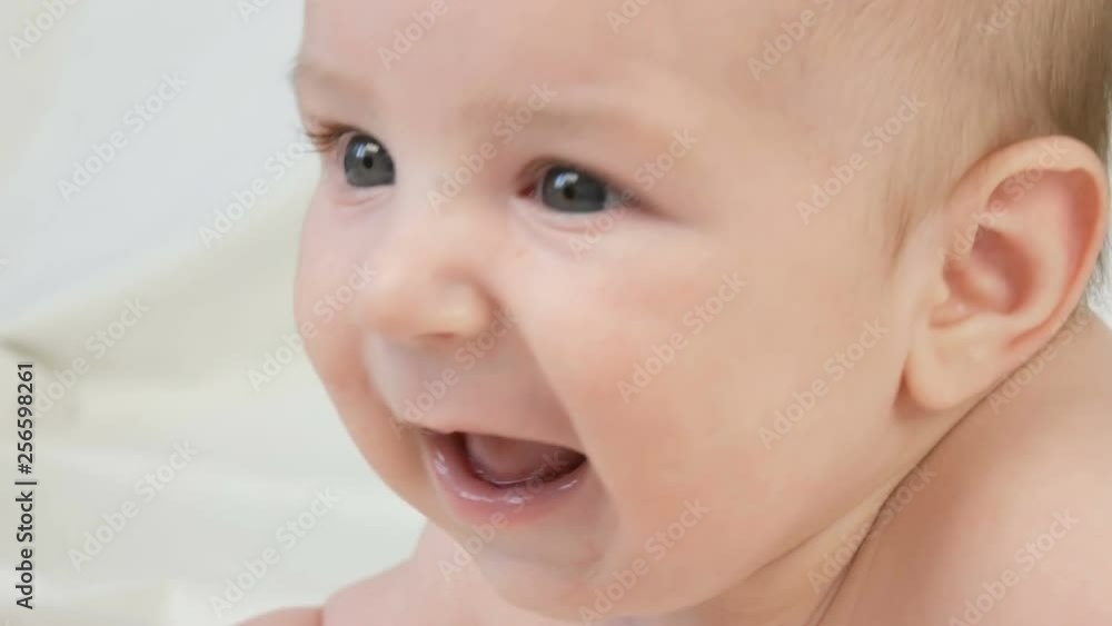 A two month old happy newborn baby lying on his stomach on the bed and experiences emotions to his mother. A baby laughs, talks, waves his arms. The child face close up view A two month old happy newborn baby lying on his stomach on the bed and experiences emotions to his mother. A baby laughs, talks, waves his arms. The child face close up view