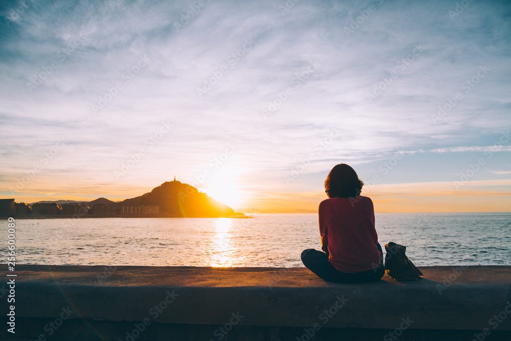 Fototapeta premium Młoda kobieta oglądając zachód słońca nad morzem w San Sebastian