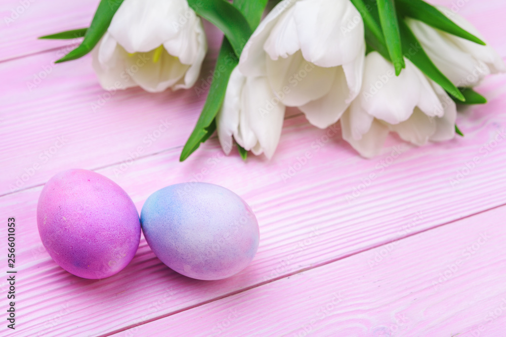 Easter background with colorful eggs and  tulips over pink wood. Top view with copy space