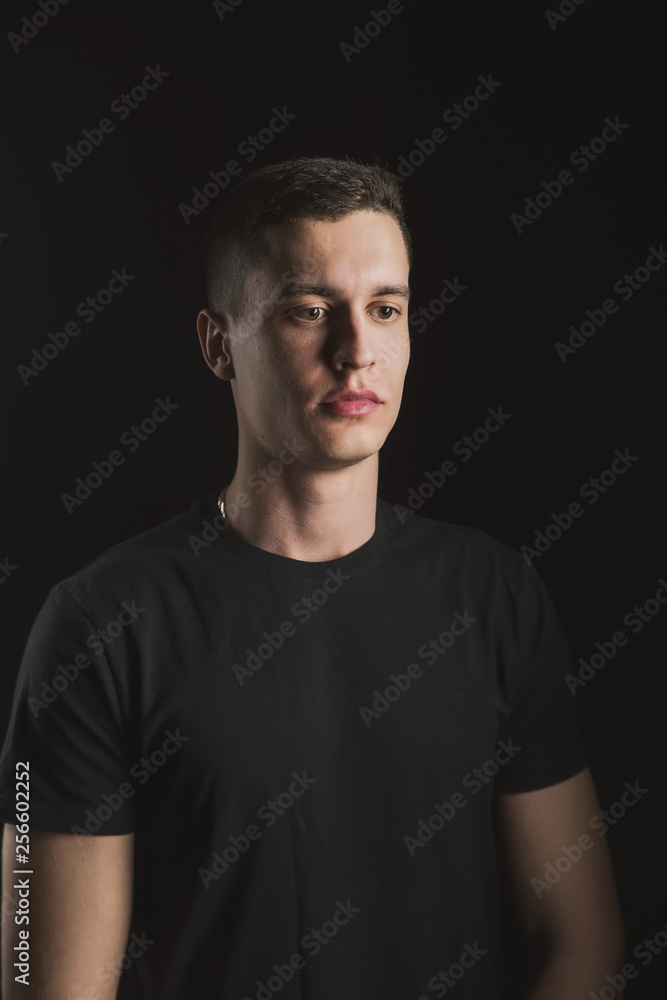Fototapeta premium Beautiful, slender young man in black t-shirt on black background and on the street