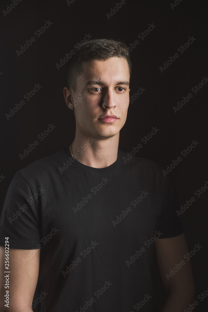Fototapeta premium Beautiful, slender young man in black t-shirt on black background and on the street