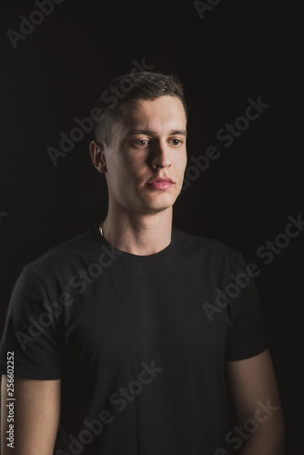 Beautiful, slender young man in black t-shirt on black background and on the street