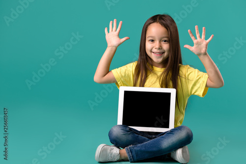 funny cute little child girl holding blank tablet computer on blue background © producer
