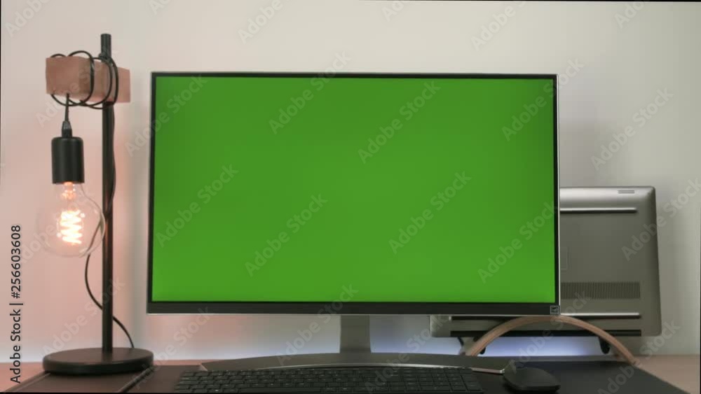 Modern monitor with green screen display standing in a desk of an office with a laptop and a lamp bulb. Modern monitor with green screen display standing in a desk of an office with a laptop and a lamp bulb.