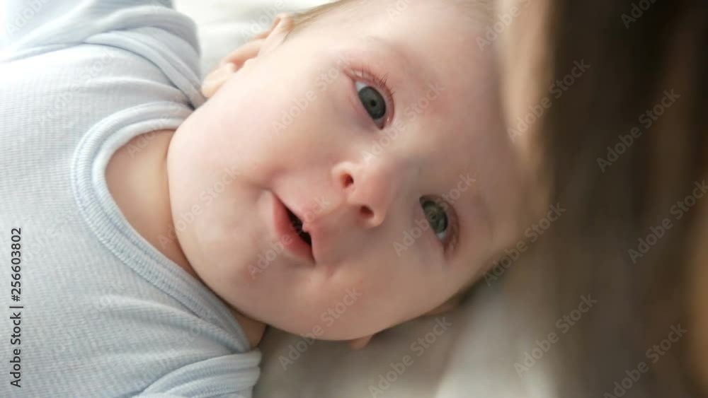 A two month old newborn happy baby lies on the bed and experiences emotions to his mother. A baby laughs, talks, waves his arms. The childs face close up view A two month old newborn happy baby lies on the bed and experiences emotions to his mother. A baby laughs, talks, waves his arms. The childs face close up view