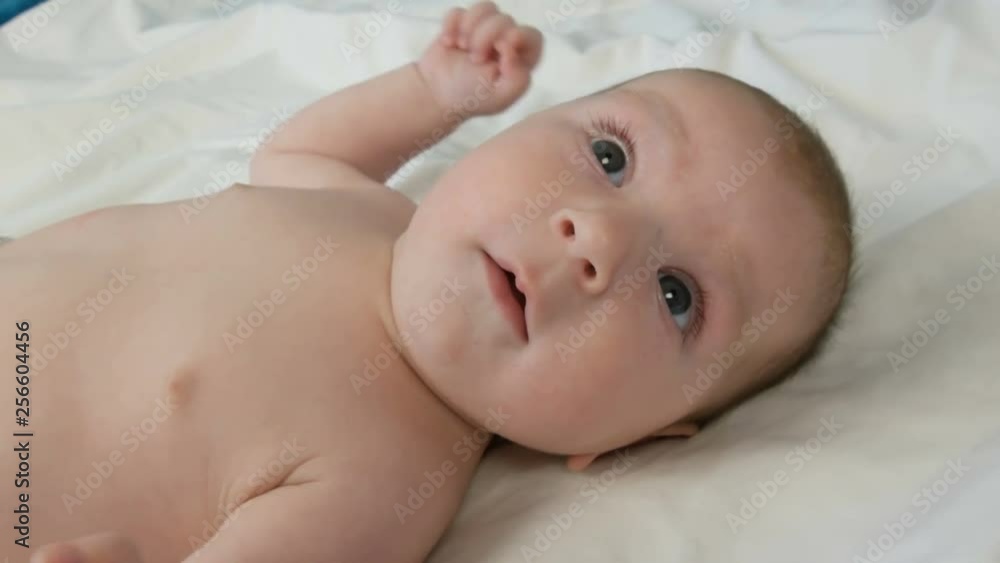 A two month old newborn happy baby lies on the bed and experiences emotions to his mother. A baby laughs, talks, waves his arms. The childs face close up view A two month old newborn happy baby lies on the bed and experiences emotions to his mother. A baby laughs, talks, waves his arms. The childs face close up view