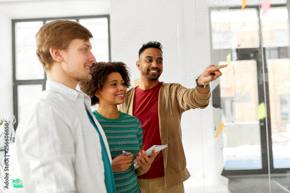 business, startup, planning and people concept - happy creative team looking at office glass board business, startup, planning and people concept - happy creative team looking at office glass board