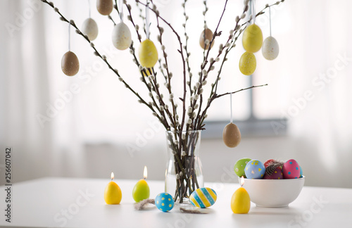 holidays and object concept - pussy willow branches decorated by easter eggs in vase and candles on table