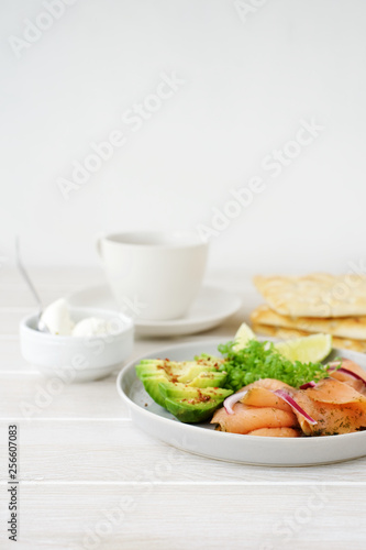 Avocado and smoked salmon on plate. Healthy breakfast. White wooden background