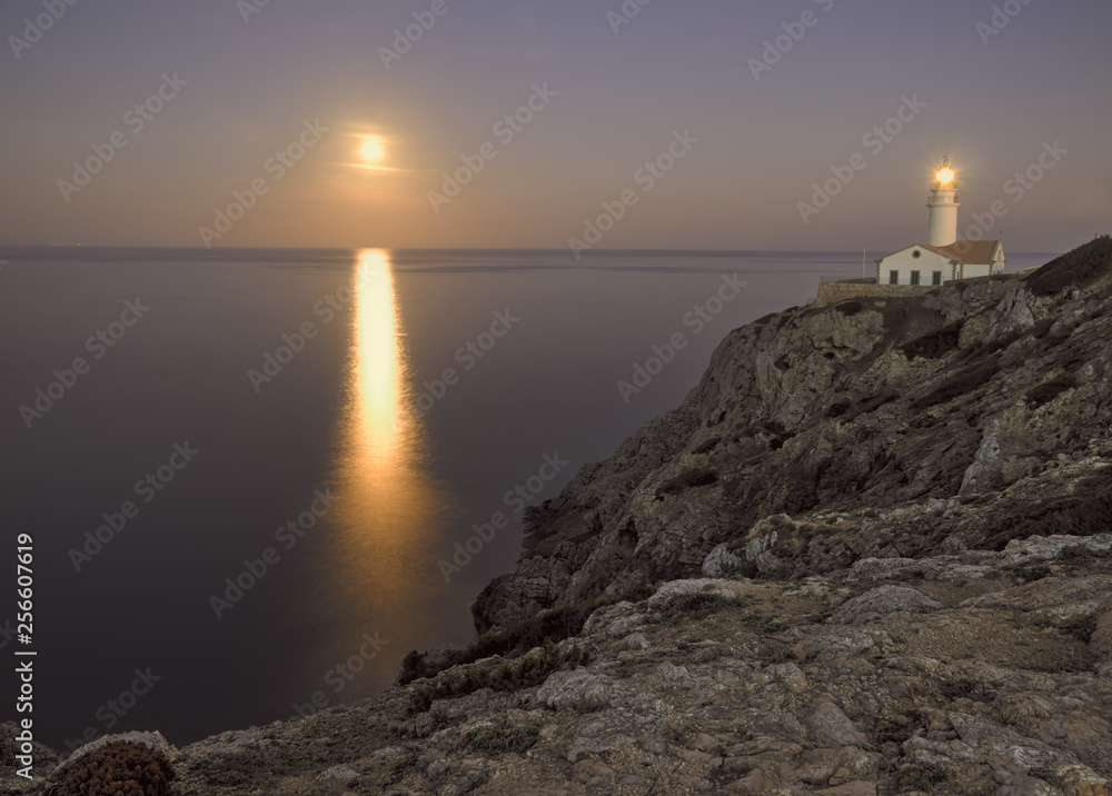 Capdepera lighthouse at dusk, with moonbeam on sea and rocks, mallorca, spain.