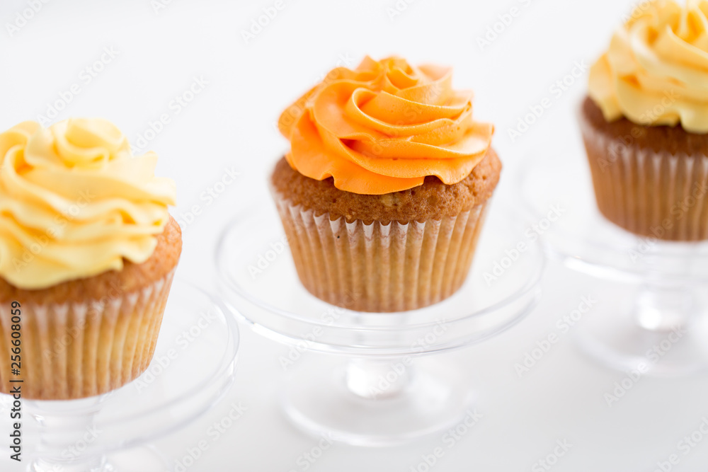 food, pastry and sweets concept - cupcakes with buttercream frosting on glass confectionery stand over white background