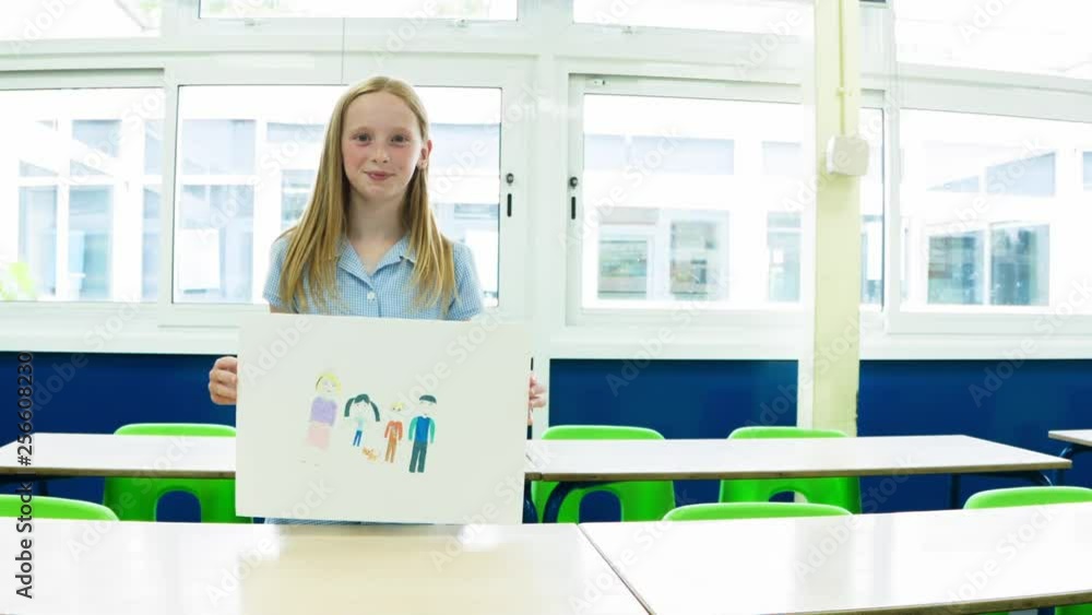 Caucasian primary school girl holding up a placard with an image of her family themes of placard family school education Caucasian primary school girl holding up a placard with an image of her family themes of placard family school education