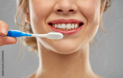 oral care, dental hygiene and people concept - close up of smiling woman with toothbrush cleaning teeth over gray background