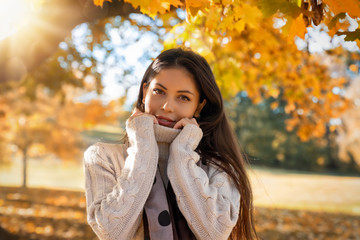 Young, attractive woman in the park during autumn time with orange leaves on the trees and golden sunshine