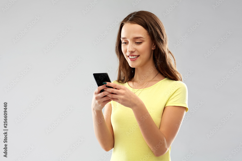 technology and people concept - smiling young woman or teenage girl in blank yellow t-shirt using smartphone over grey background technology and people concept - smiling young woman or teenage girl in blank yellow t-shirt using smartphone over grey background