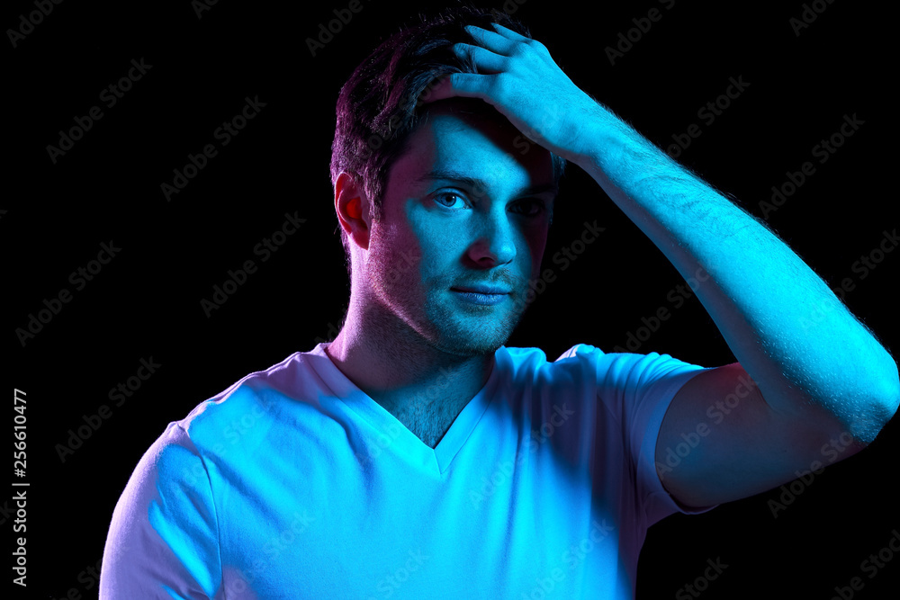 people concept - portrait of young man in t-shirt touching his hair over ultra violet neon lights in dark room people concept - portrait of young man in t-shirt touching his hair over ultra violet neon lights in dark room