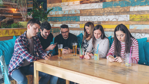 Foto Group of friends at restaurant ignoring each other in favour of mobile phone - p