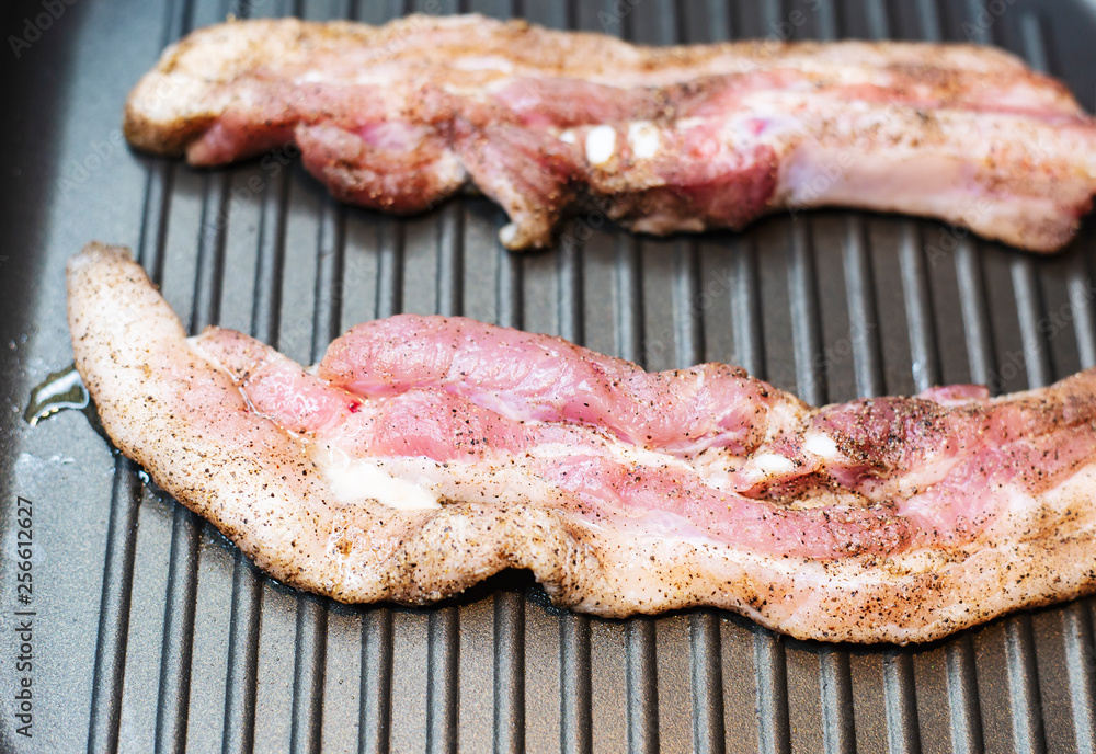 Two pieces of pork meat sprinkled with pepper, fry in a frying pan on one side. Two pieces of pork meat sprinkled with pepper, fry in a frying pan on one side.