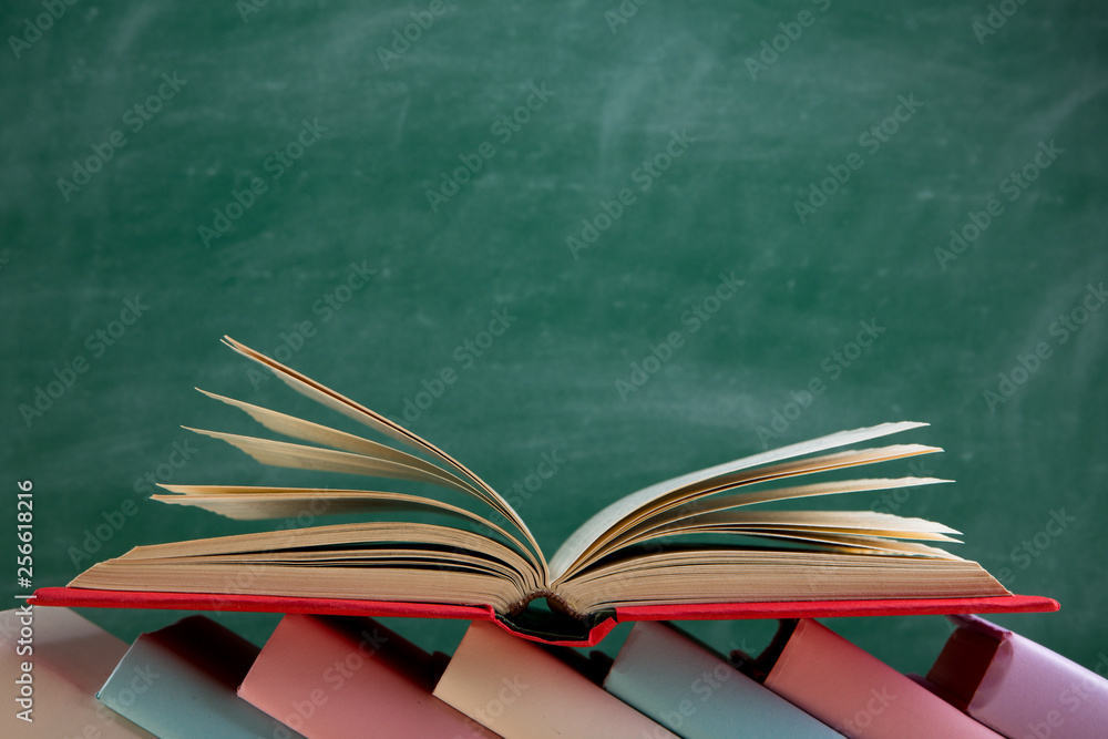 Naklejka premium Education and reading concept - group of colorful books on the wooden table in the classroom, blackboard background