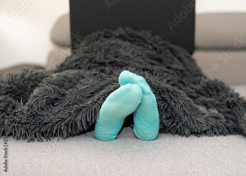 Frau stitzt auf der Couch mit dem Laptop und man sieht die Füße