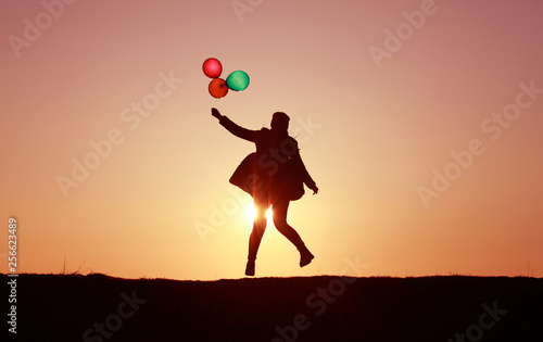 girl flies with balloons at sunset, multi-colored balloons, incredible sky sunset, flying into the sky