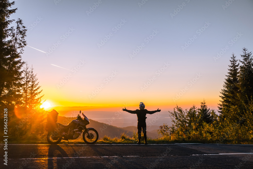 Silhouette of man biker and adventure motorcycle on the road with sunset light. Hands up. enjoy momment. Top of mountains, tourism motorbike, vacation active lifestyle. Transfagarasan, Romania.