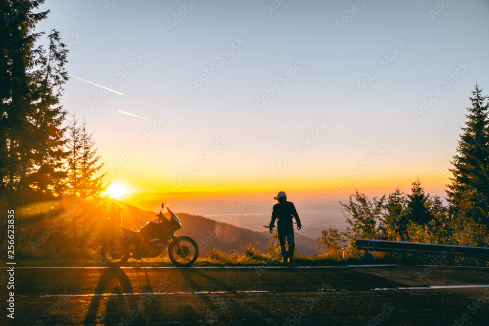 Fototapeta premium Silhouette of man biker and adventure motorcycle on the road with sunset light background. Top of mountains, tourism motorbike, vacation active lifestyle. Transfagarasan, Romania.