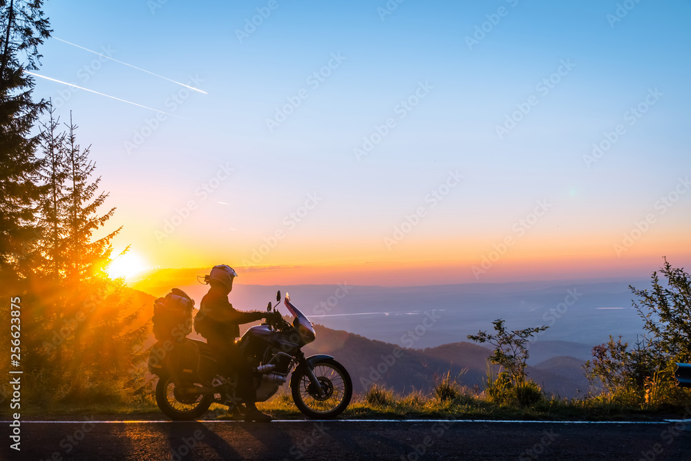 Silhouette of man biker and adventure motorcycle on the road with sunset light background. Top of mountains, tourism motorbike, vacation active lifestyle. Transfagarasan, Romania.