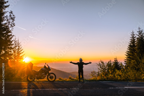 Silhouette of man biker and adventure motorcycle on the road with sunset light. Hands up. enjoy momment. Top of mountains, tourism motorbike, vacation active lifestyle. Transfagarasan, Romania. © Sergey